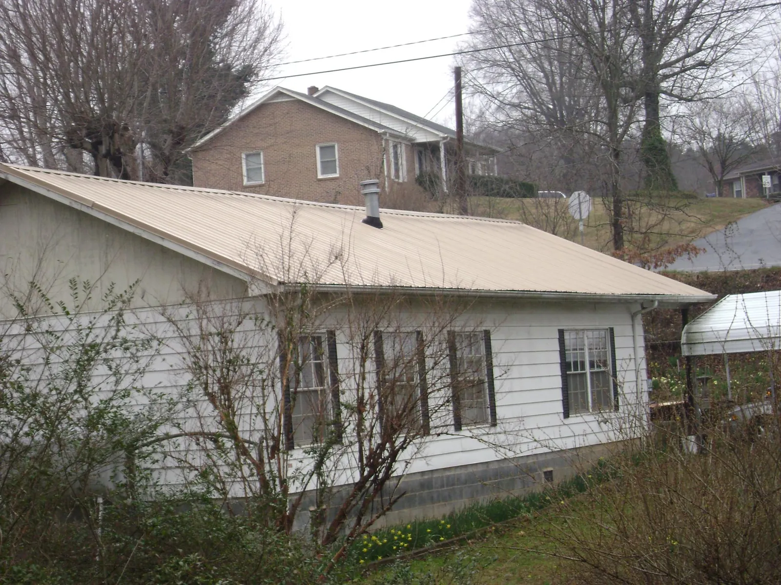 Tan metal roof on a white sided house set into a hillside — Commercial Roofing by Roofing Brothers in Washington Navy Yard
